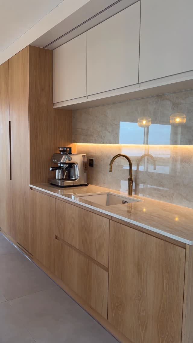 Modern kitchen with light wood cabinets, white upper cupboards, and marble surfaces.