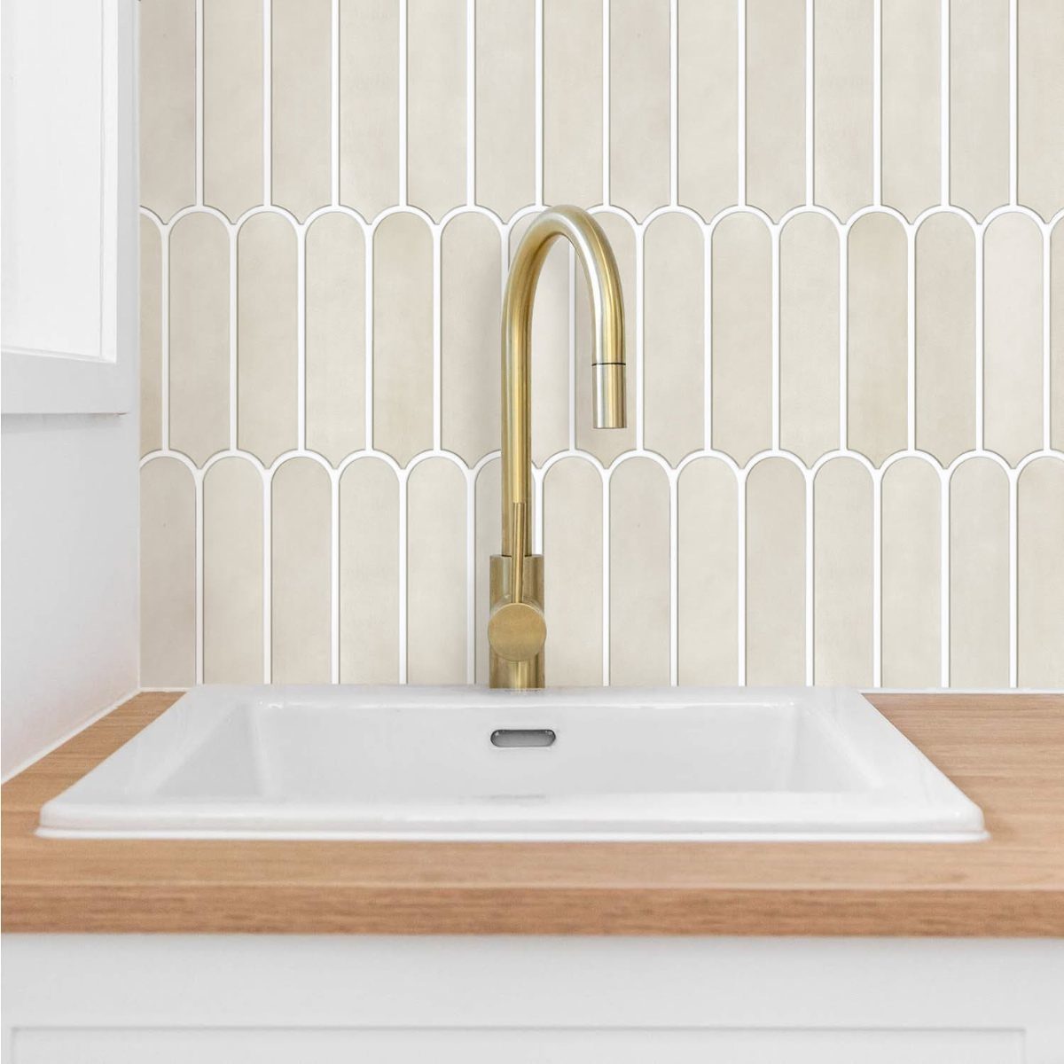 Cream arched tile backsplash behind a white sink with a gold faucet
