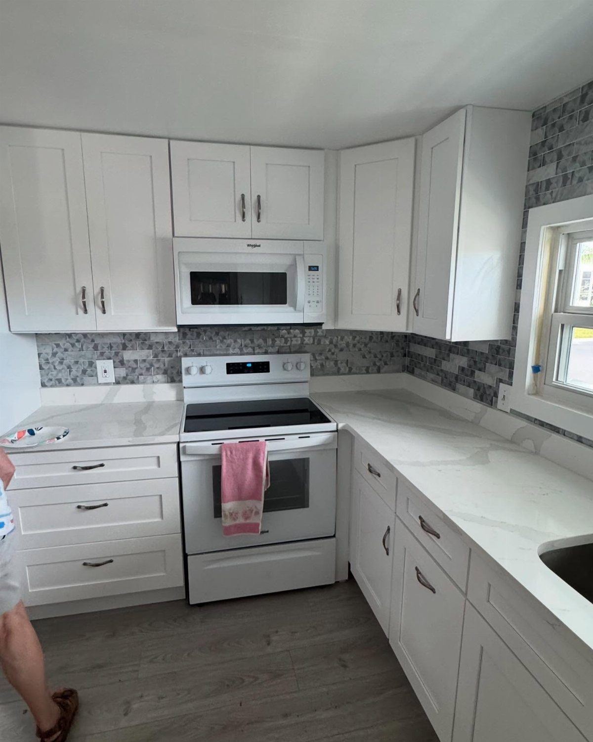 White kitchen cabinets and countertops with a grey and white mosaic tile backsplash.