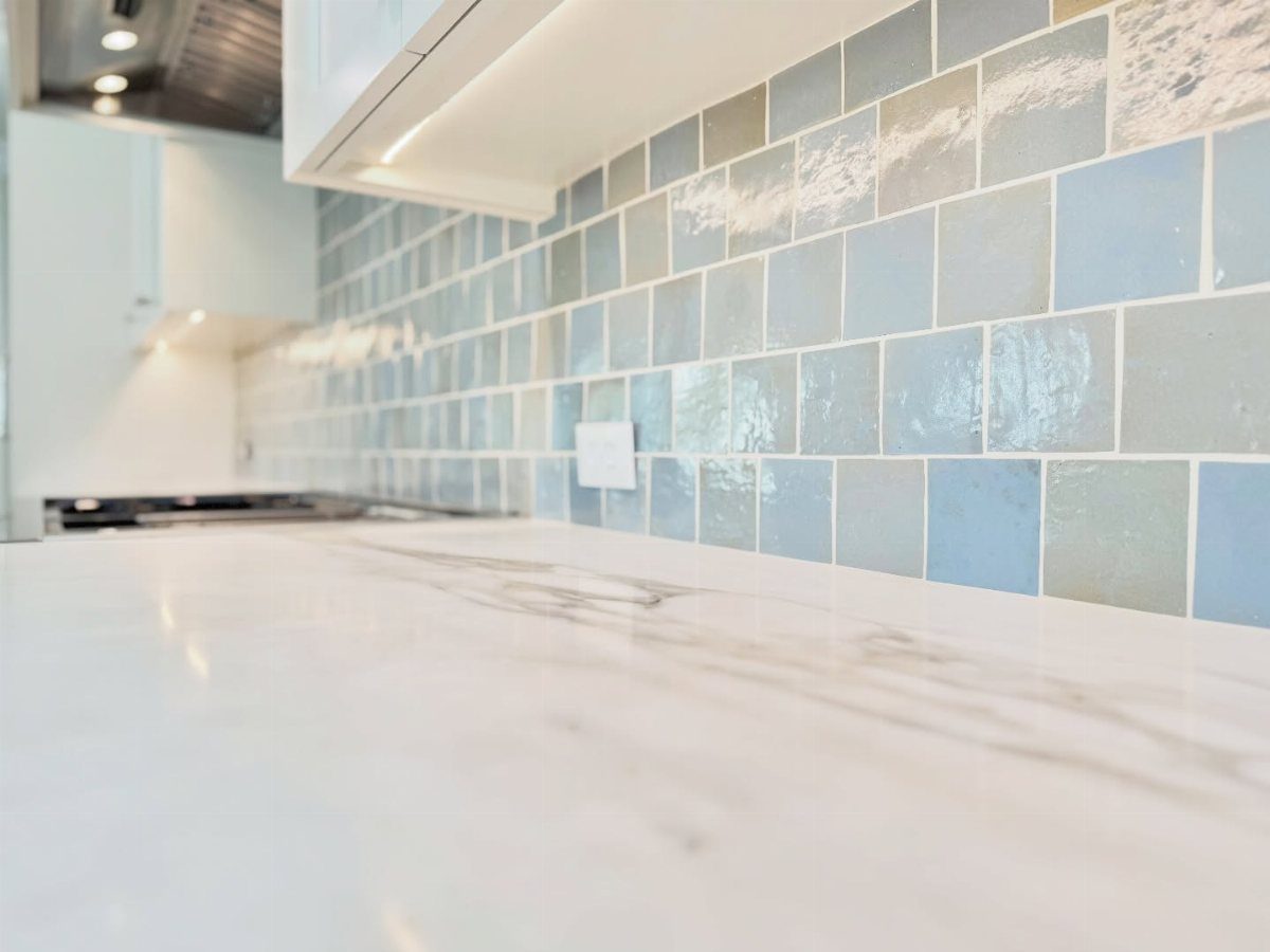 Light blue handcrafted zellige tile backsplash with white marble countertops and white cabinets.