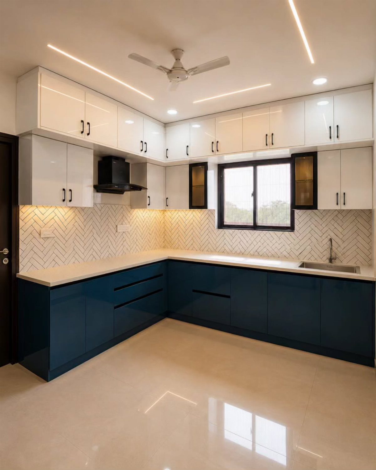 White herringbone tile backsplash between white upper and dark blue lower kitchen cabinets.