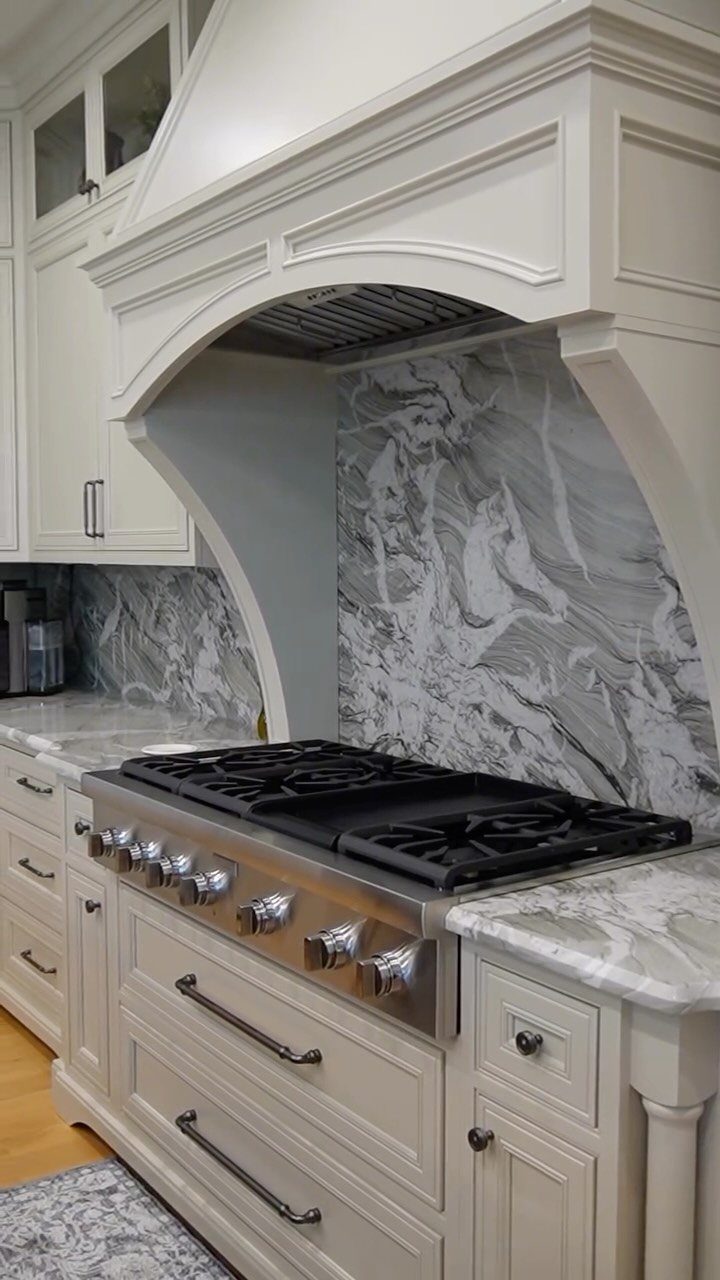 White marble backsplash with grey veining behind a professional gas range and white cabinets