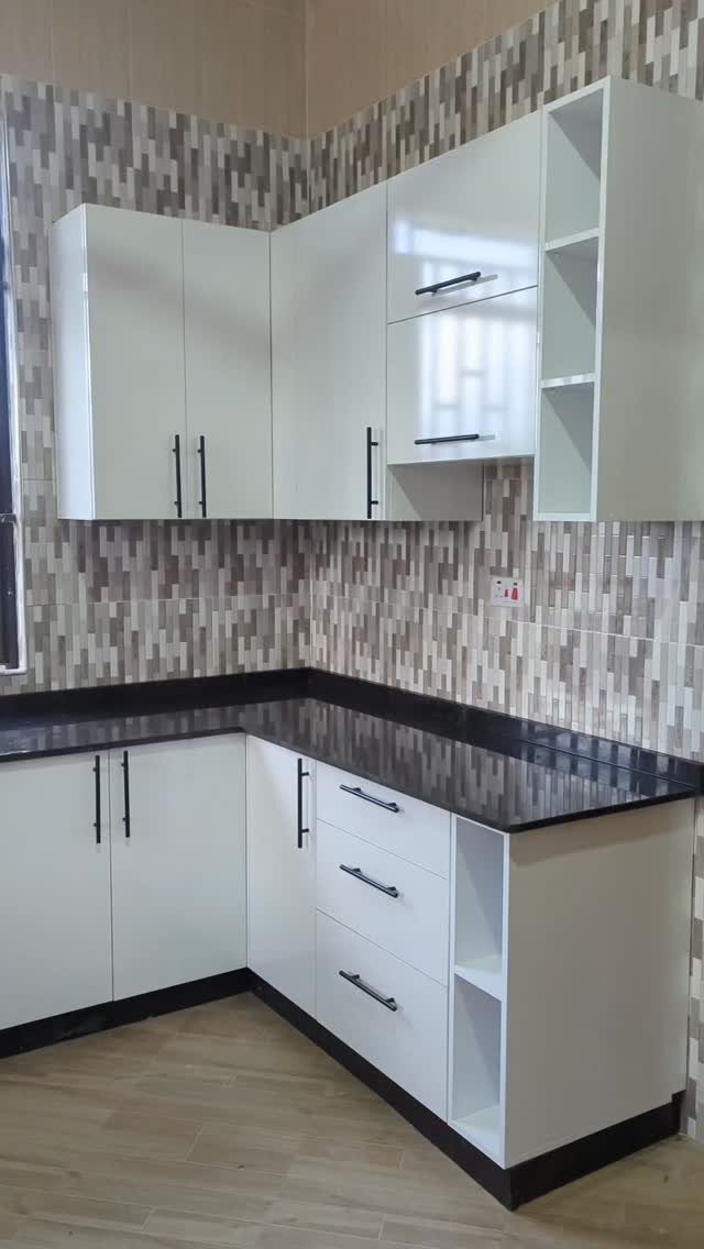 White kitchen cabinets with a black countertop and grey multi-toned tile backsplash.