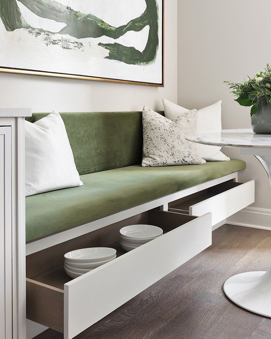 Green upholstered kitchen banquette with two open white storage drawers containing white bowls.