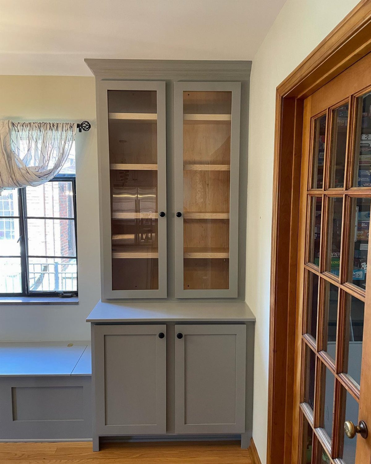 Grey built-in kitchen banquette seating and matching hutch cabinet in a bright room.