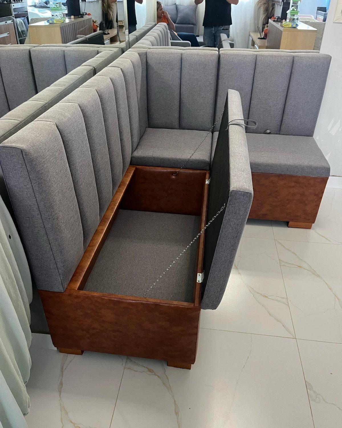 Grey L-shaped banquette with a lift-top seat revealing under-seat storage in wooden base.