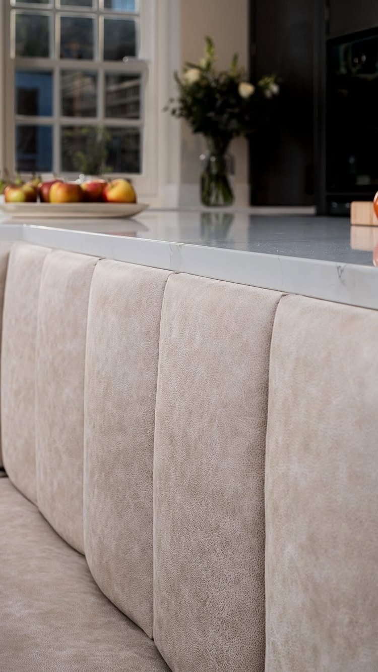 Beige upholstered channel-tufted banquette seating next to a white marble kitchen counter.