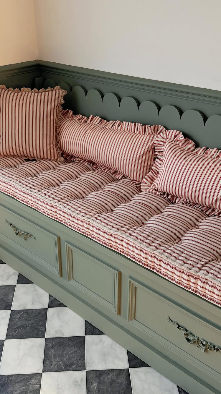 Sage green built-in bench with red and white striped cushions and drawers.