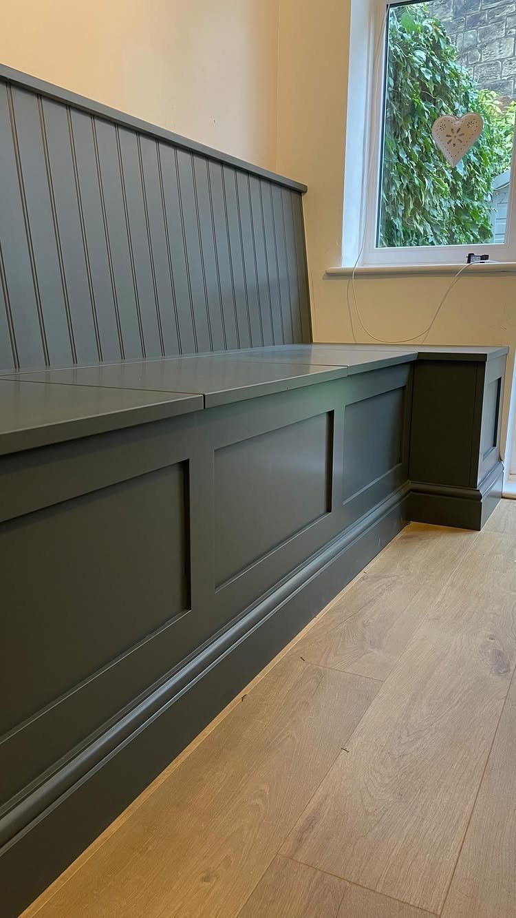 Grey built-in wooden bench with paneled base and high backrest against a wall.