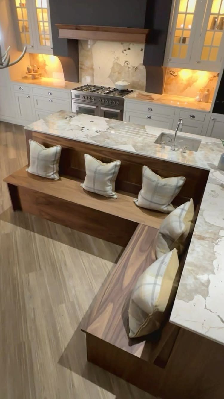 L-shaped wooden built-in bench with pillows next to a marble kitchen island