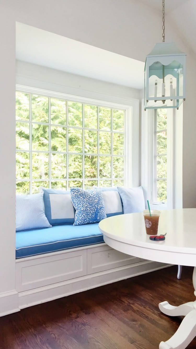 White built-in kitchen bench with blue cushions and patterned pillows by a window.