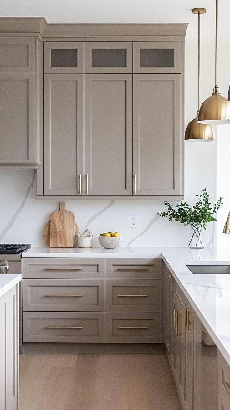 Taupe kitchen cabinets with gold hardware and white countertops in a modern kitchen.