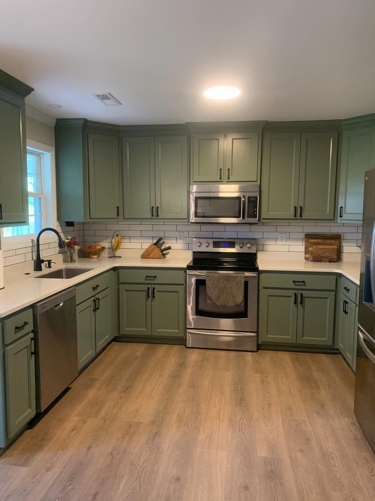 Sage green kitchen cabinets with white countertops and stainless steel appliances.