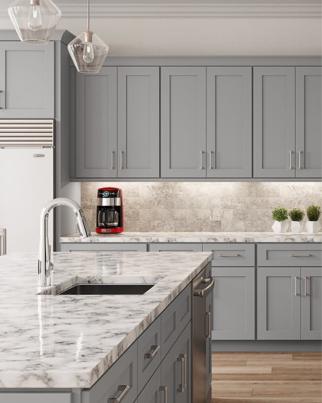 Grey shaker-style kitchen cabinets with white marble countertops and a red coffee maker.