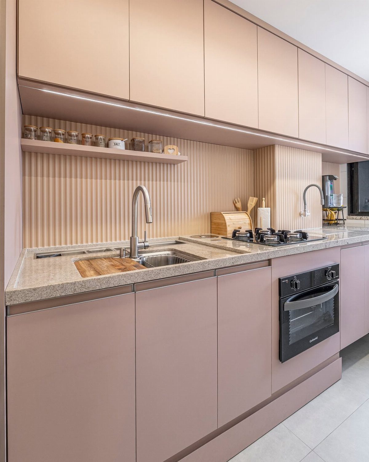 Dusty rose kitchen cabinets with a light speckled stone countertop and black oven.