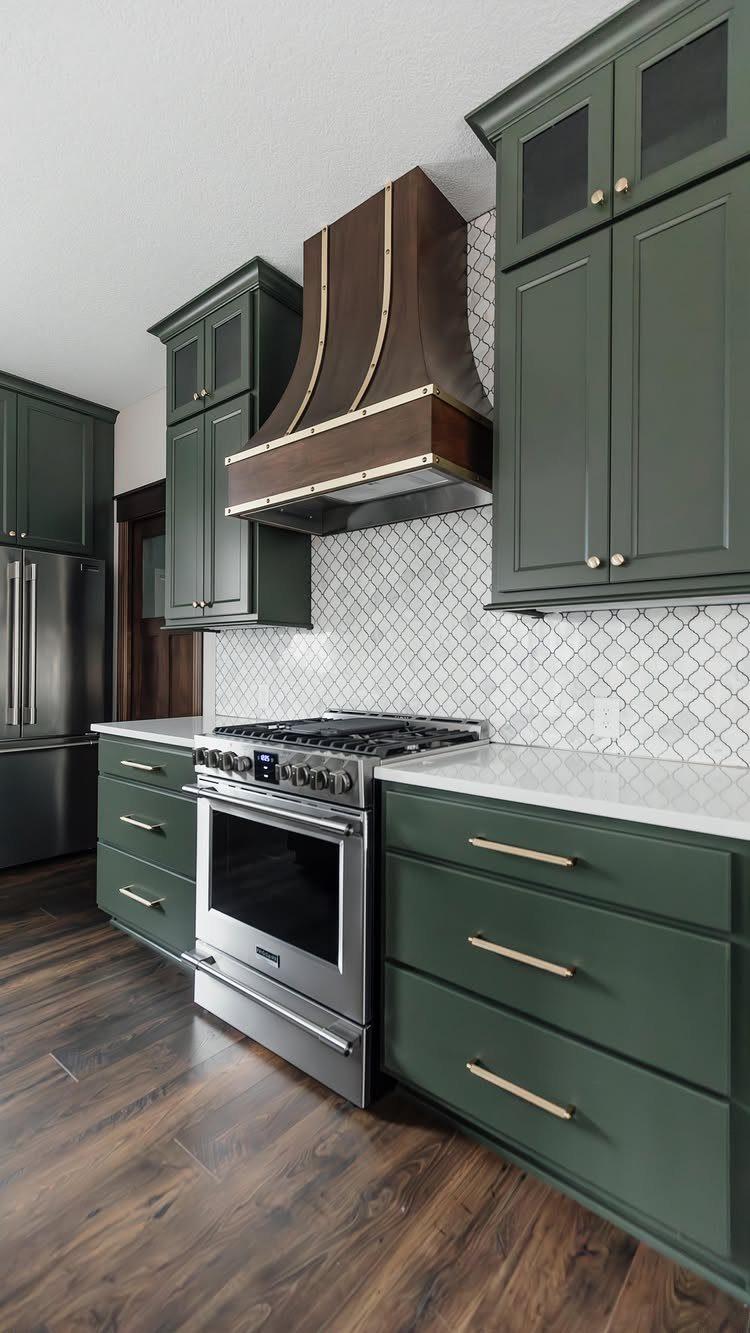 Dark green kitchen cabinets with gold hardware and a wooden range hood.