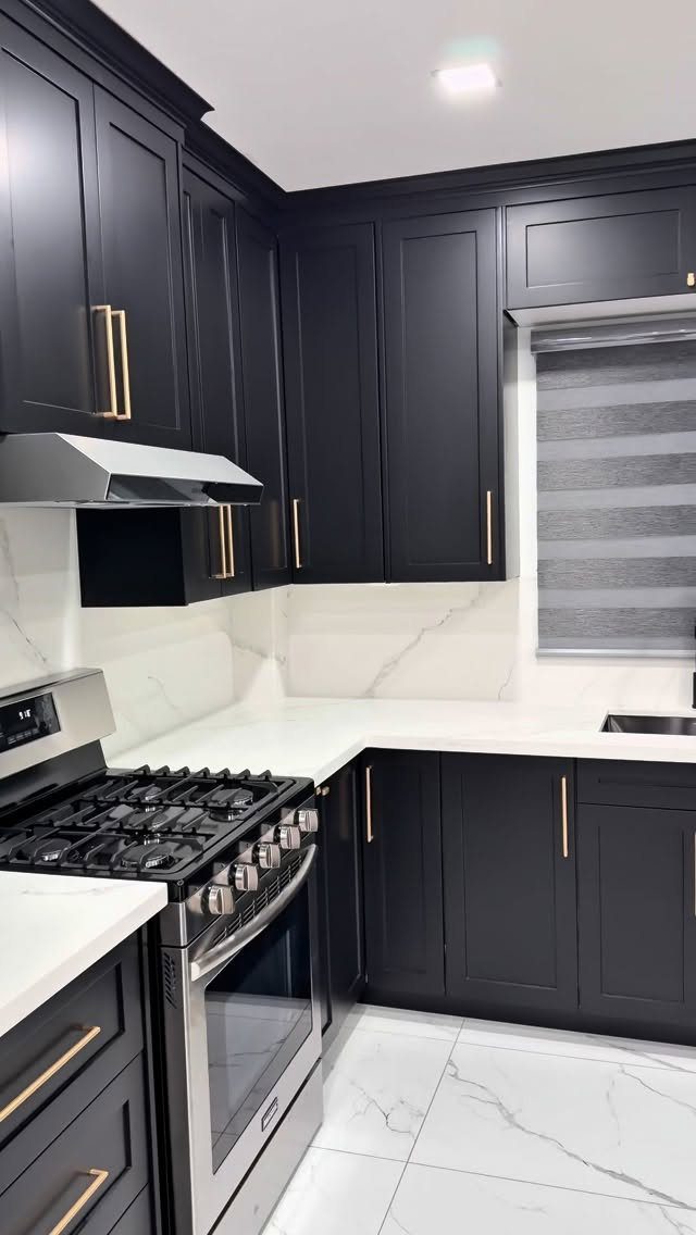 Matte black kitchen cabinets with gold hardware and white marble countertops.