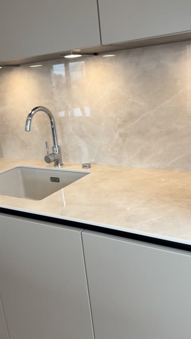 Grey handleless kitchen cabinets with a beige marble countertop and chrome faucet.