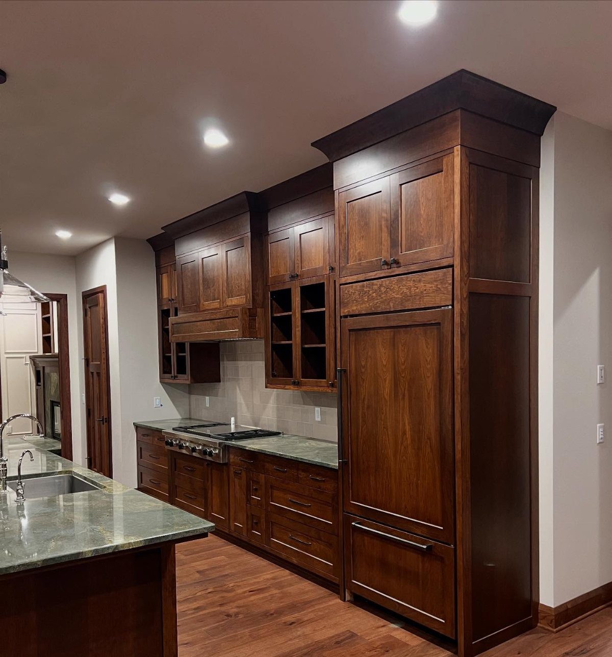 Cherry wood kitchen cabinets paired with gray quartz countertops and hardwood flooring.