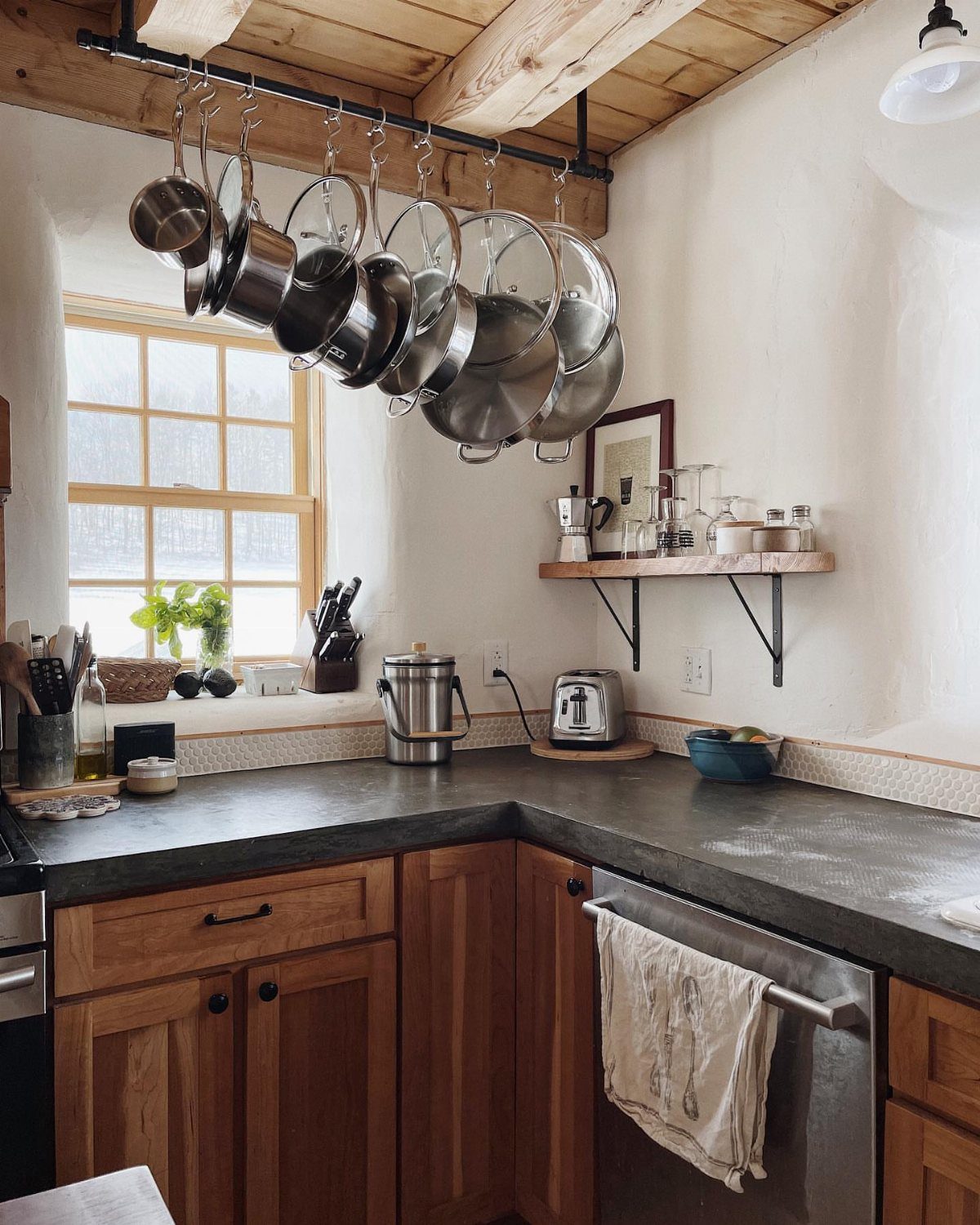 Grey concrete countertops paired with warm wood cabinets and hanging stainless steel pots.