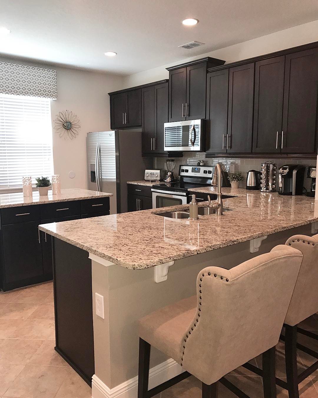 Dark espresso kitchen cabinets with speckled granite countertops and beige bar stools.