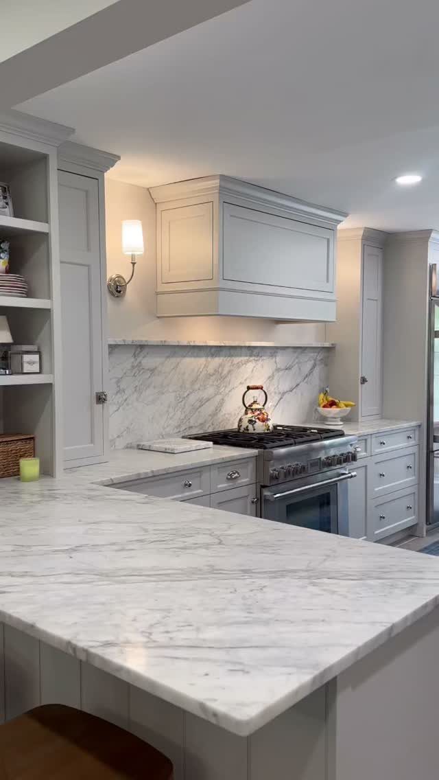 White marble-look countertops and backsplash with light gray kitchen cabinets and stainless stove.