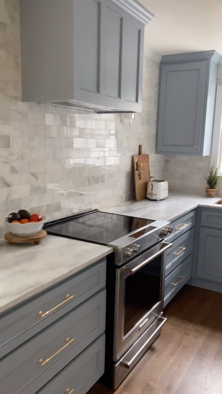 Muted blue kitchen cabinets with white quartz countertops and gold hardware.