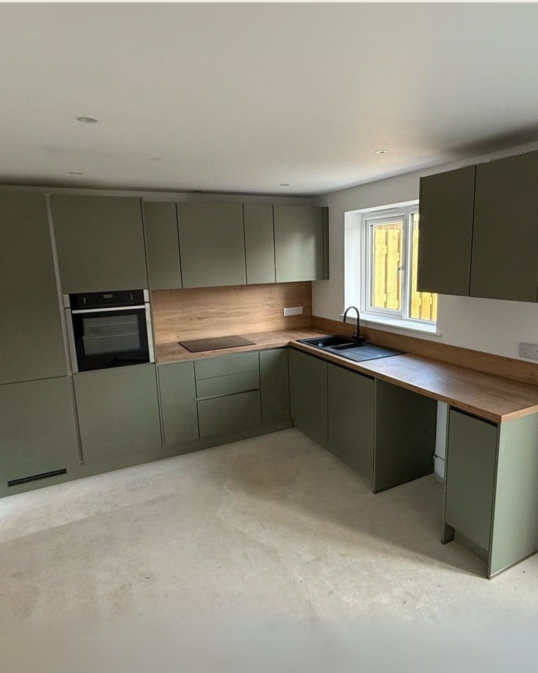 Olive green kitchen cabinets paired with light wood countertops and light flooring.