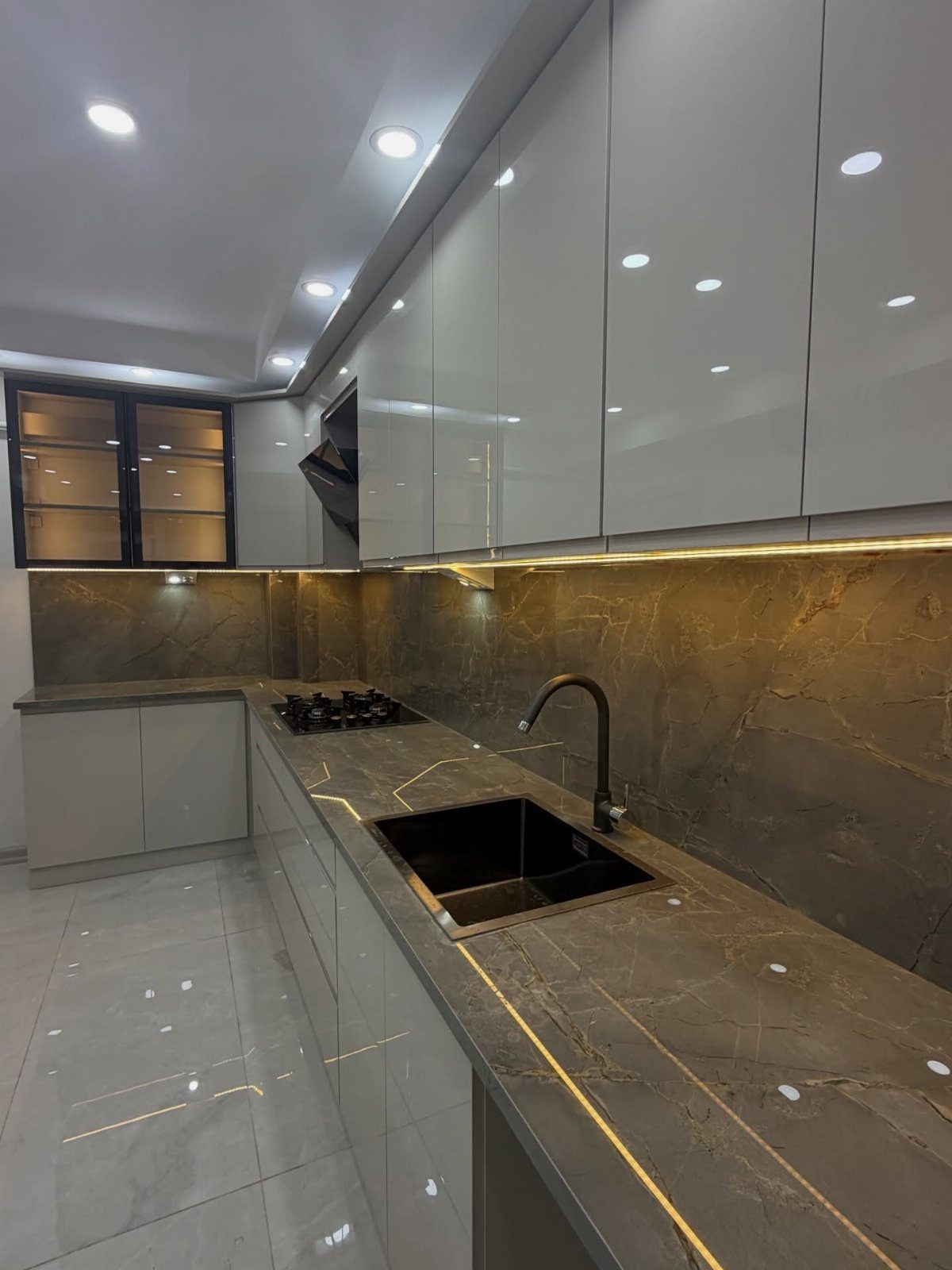 Polished grey veined porcelain countertops and backsplash with glossy white kitchen cabinets.