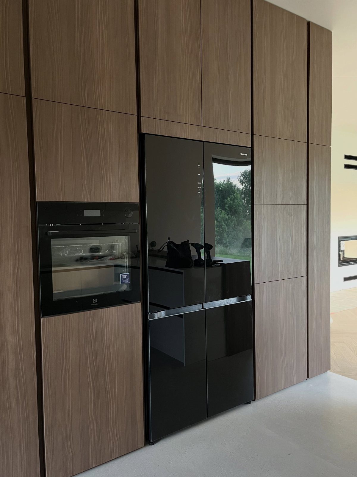 Light brown wood kitchen cabinets with integrated black oven and glossy black refrigerator.