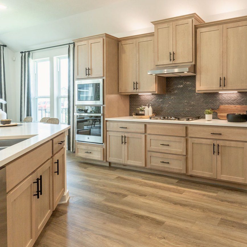 Light wood kitchen cabinets with white countertops and a dark grey backsplash.