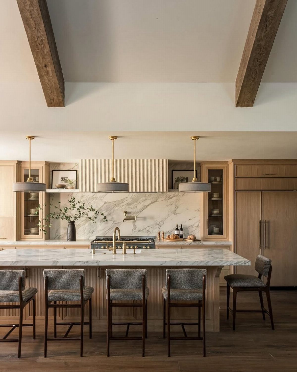 Light wood kitchen cabinets with white marble countertops and dark wood ceiling beams.