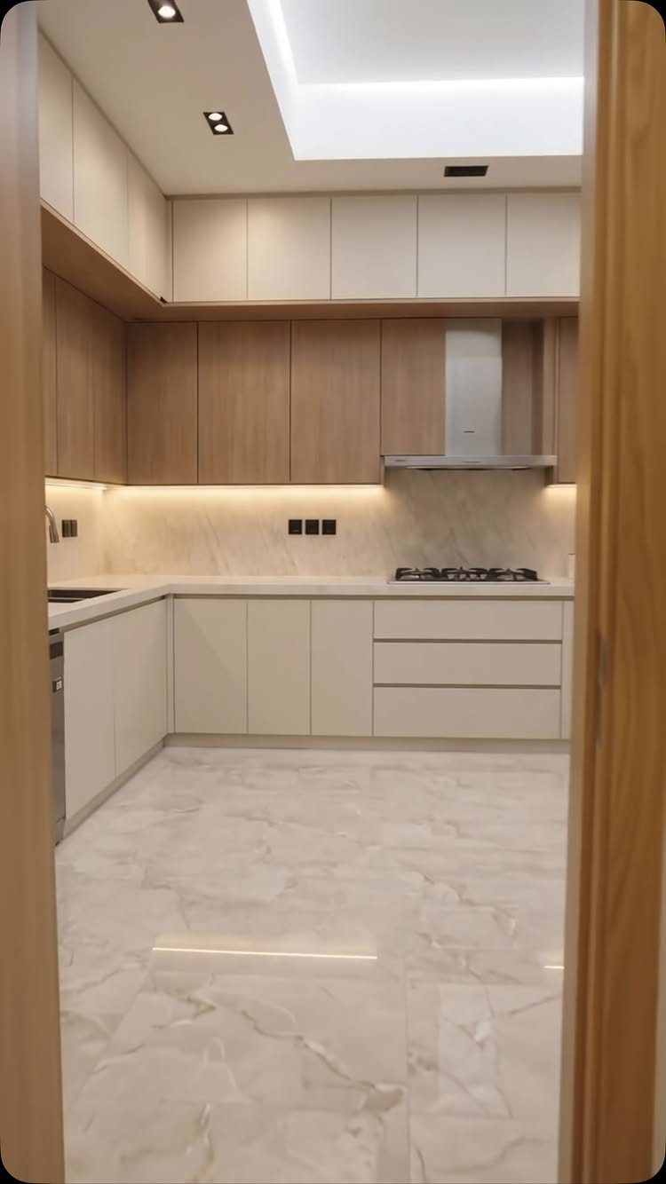 Modern kitchen with light wood upper cabinets, white lower cabinets, and marble flooring.