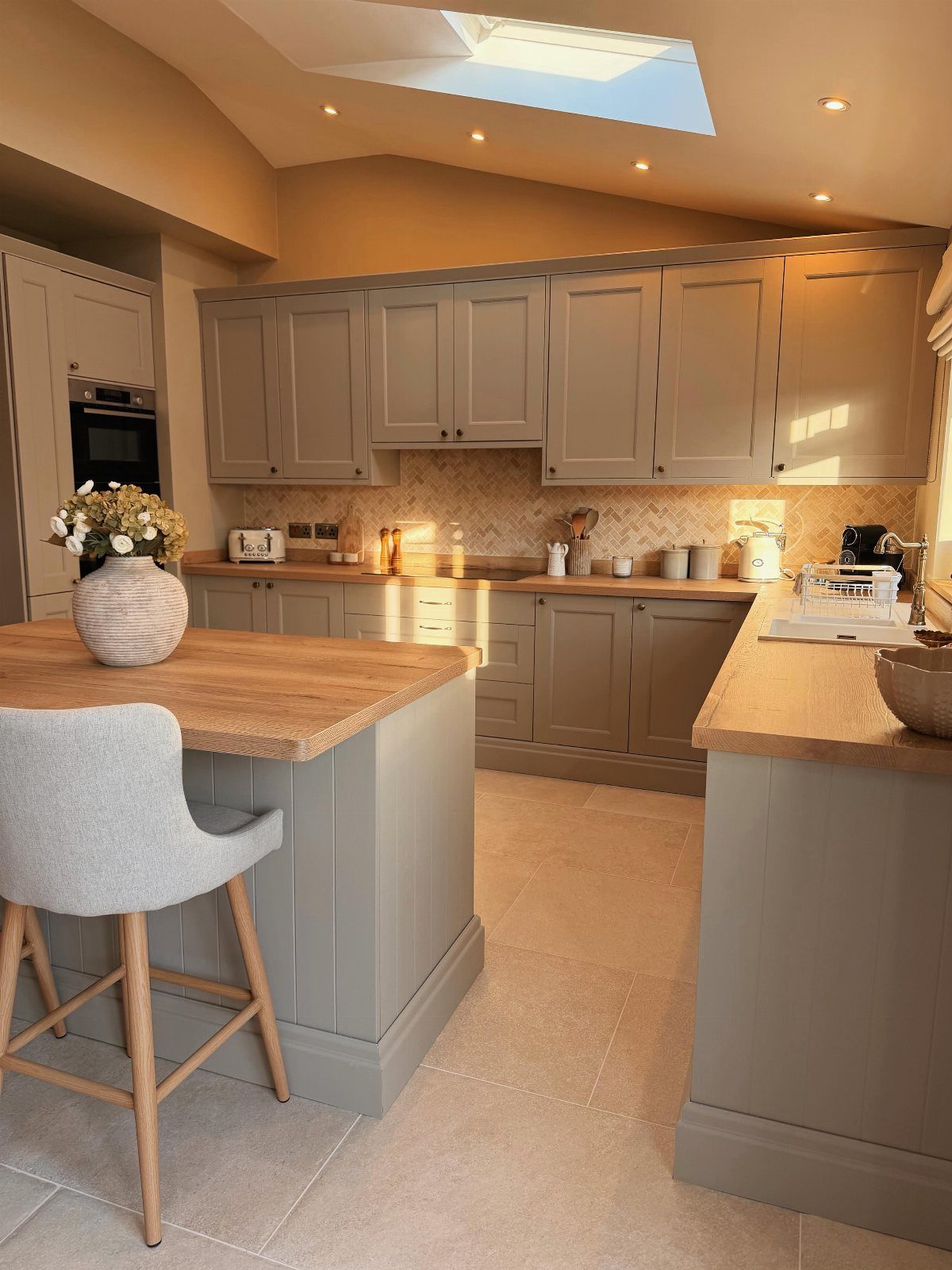 Taupe-grey kitchen cabinets with light wood countertops and a matching center island.