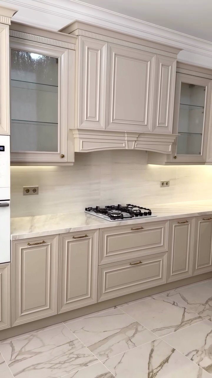 Light beige wooden kitchen cabinets with white marble countertops and built-in gas stovetop.