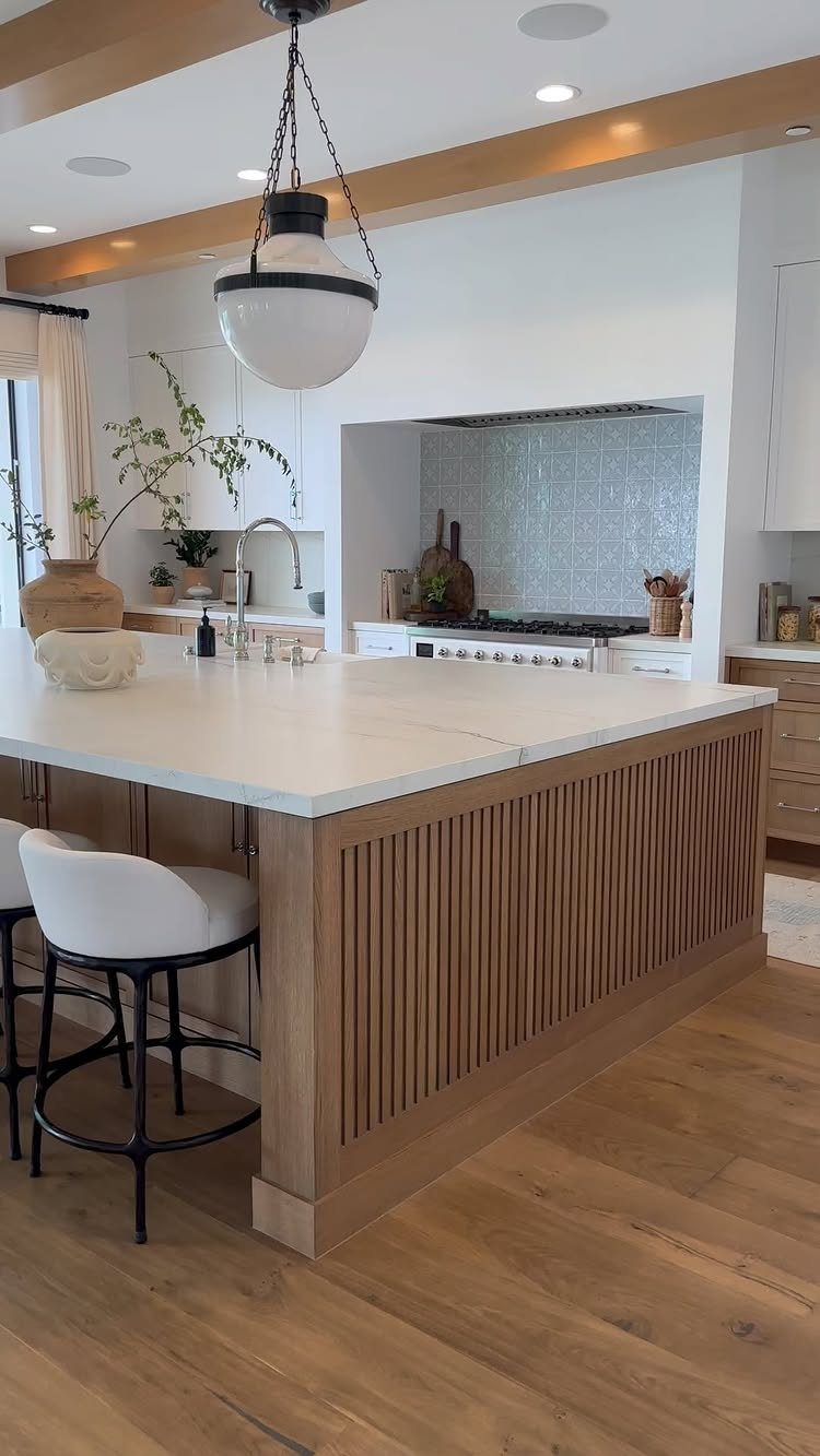 Light wood kitchen island with white countertops and a modern pendant light fixture.