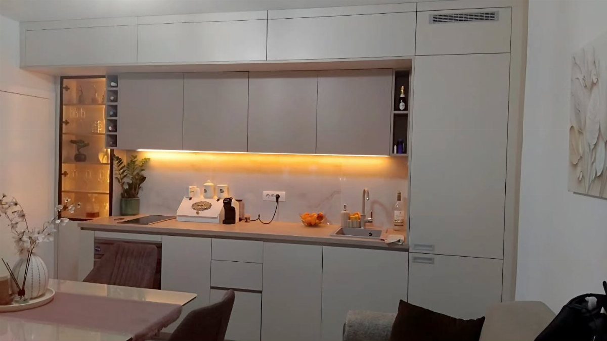 Off-white kitchen cabinets with warm under-cabinet lighting illuminating a light-colored countertop.