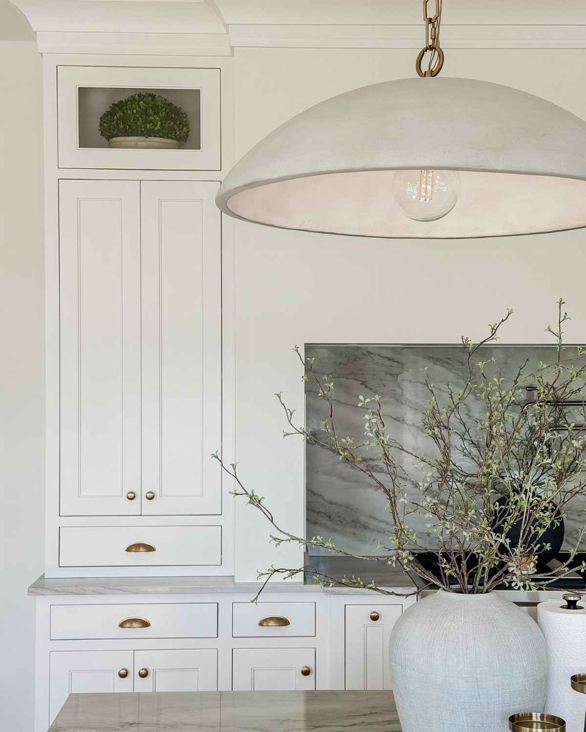 Off-white kitchen cabinets with gold hardware and a large white dome pendant light.