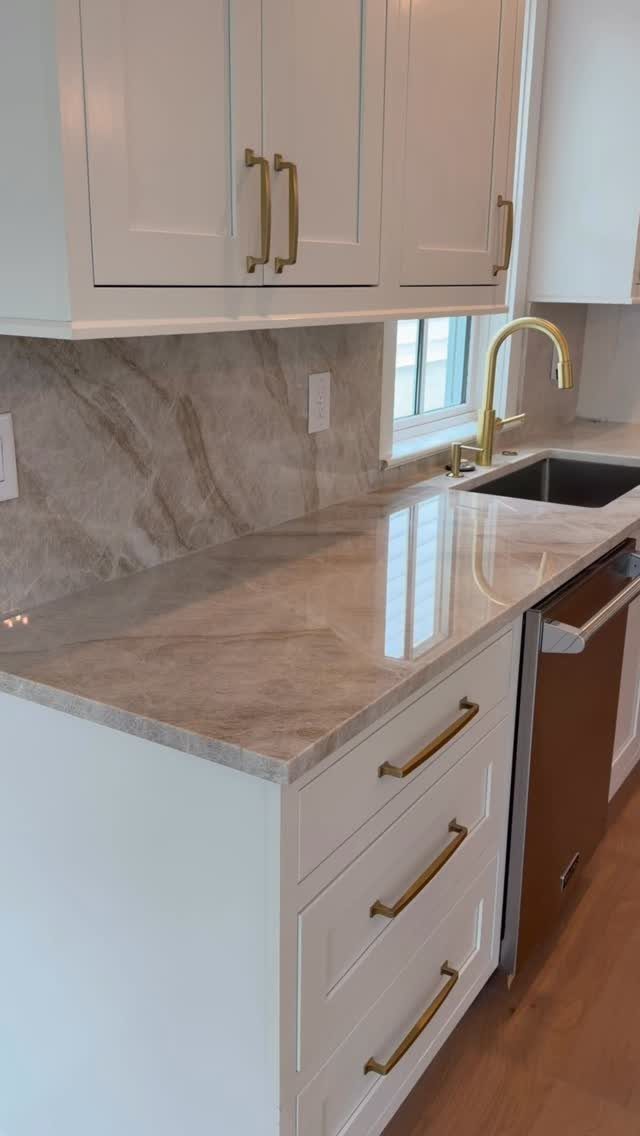 White kitchen cabinets with gold hardware and a marbled brown countertop and backsplash.