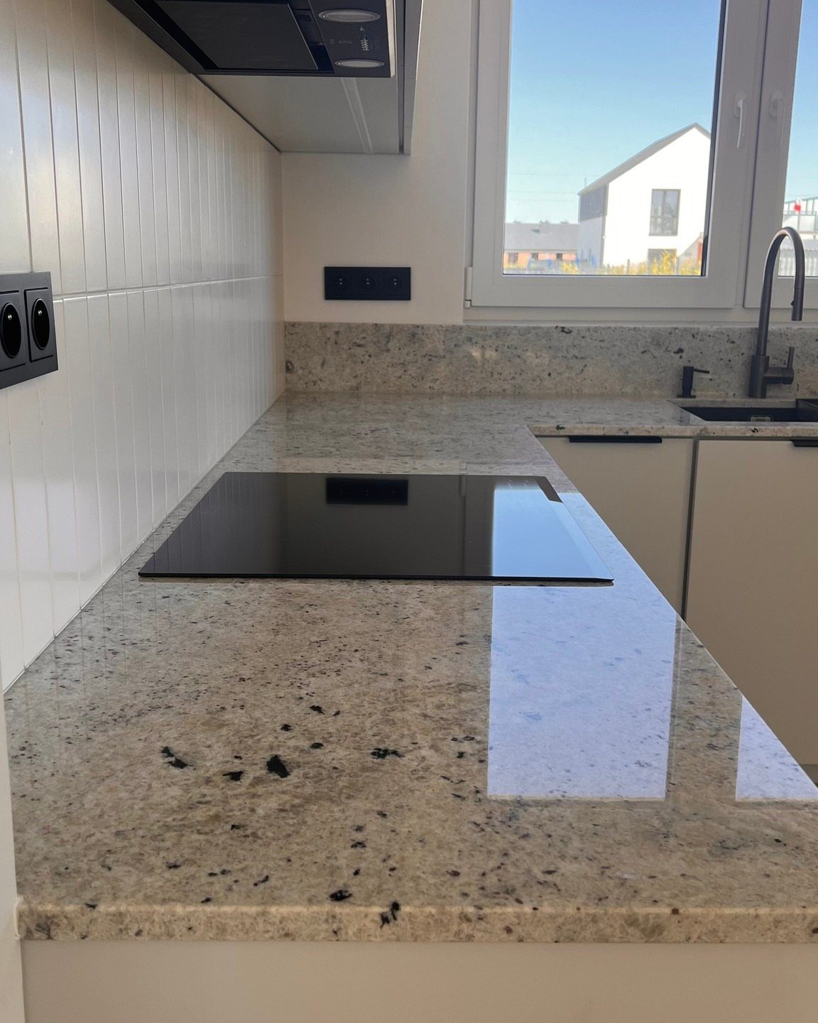 Speckled granite countertops in a kitchen with white cabinets and a black stovetop.