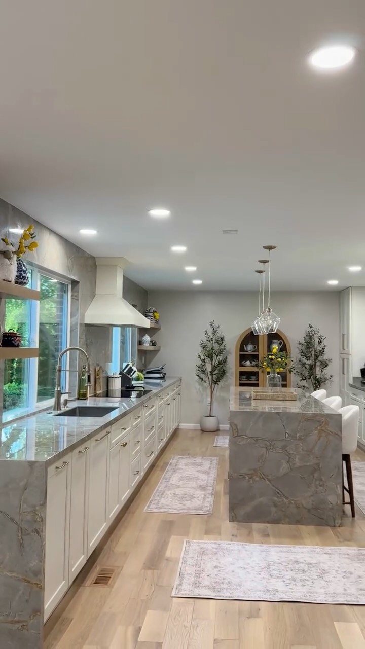 Grey-veined marble countertops and white cabinets in a bright, modern kitchen with wood floors.