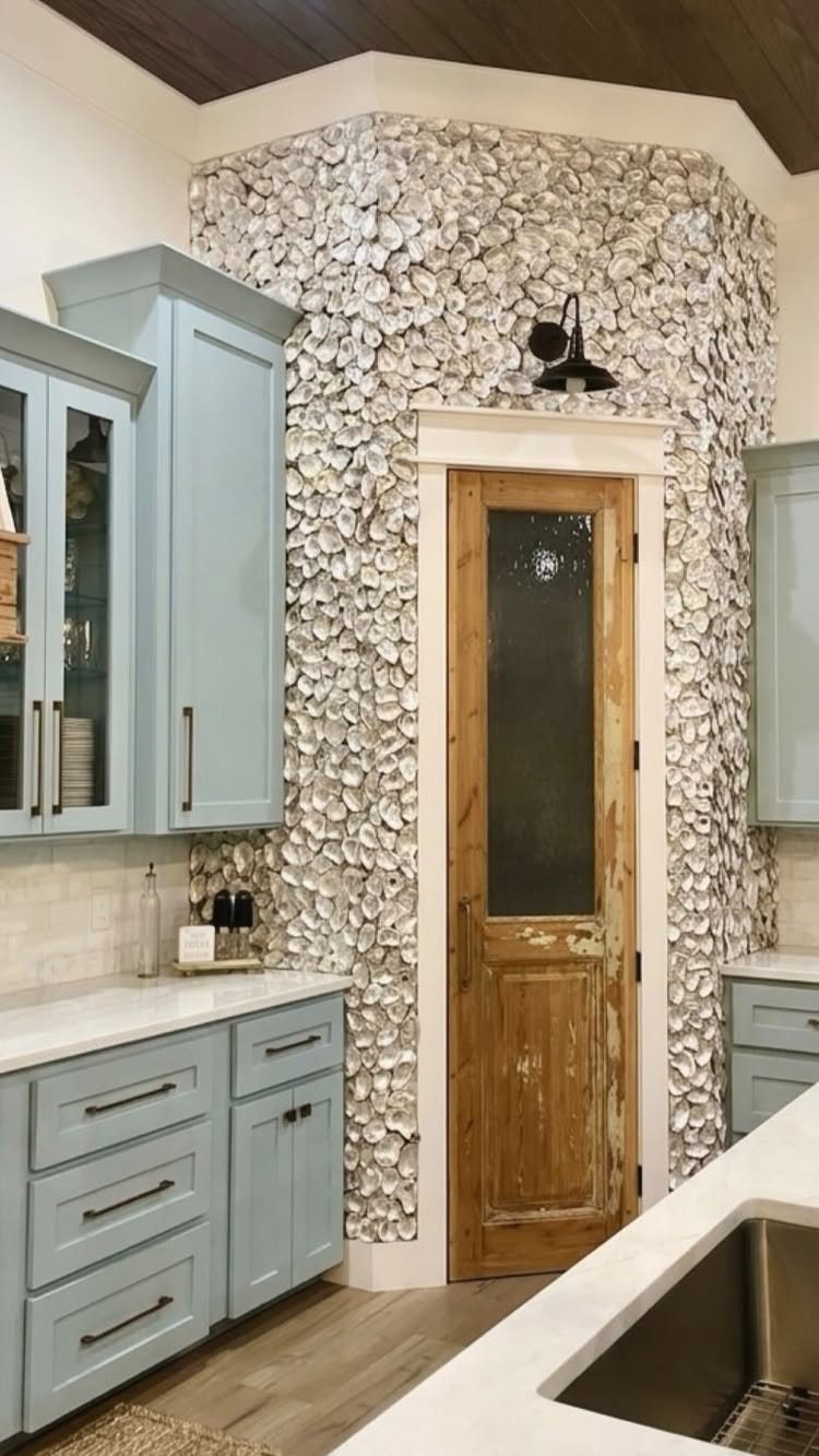Light blue kitchen cabinets and a seashell mosaic wall surrounding a wooden door.