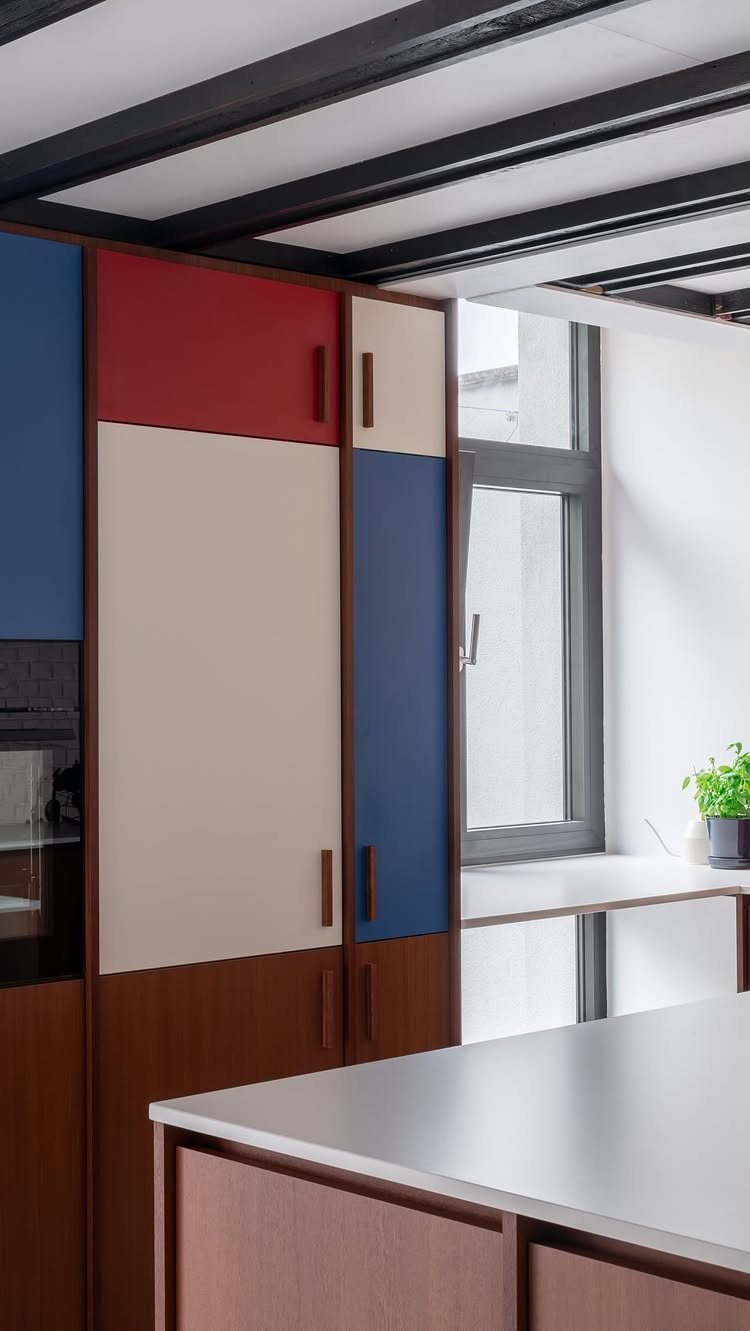 Color-blocked kitchen cabinets in red, blue, and beige with dark wood framing.