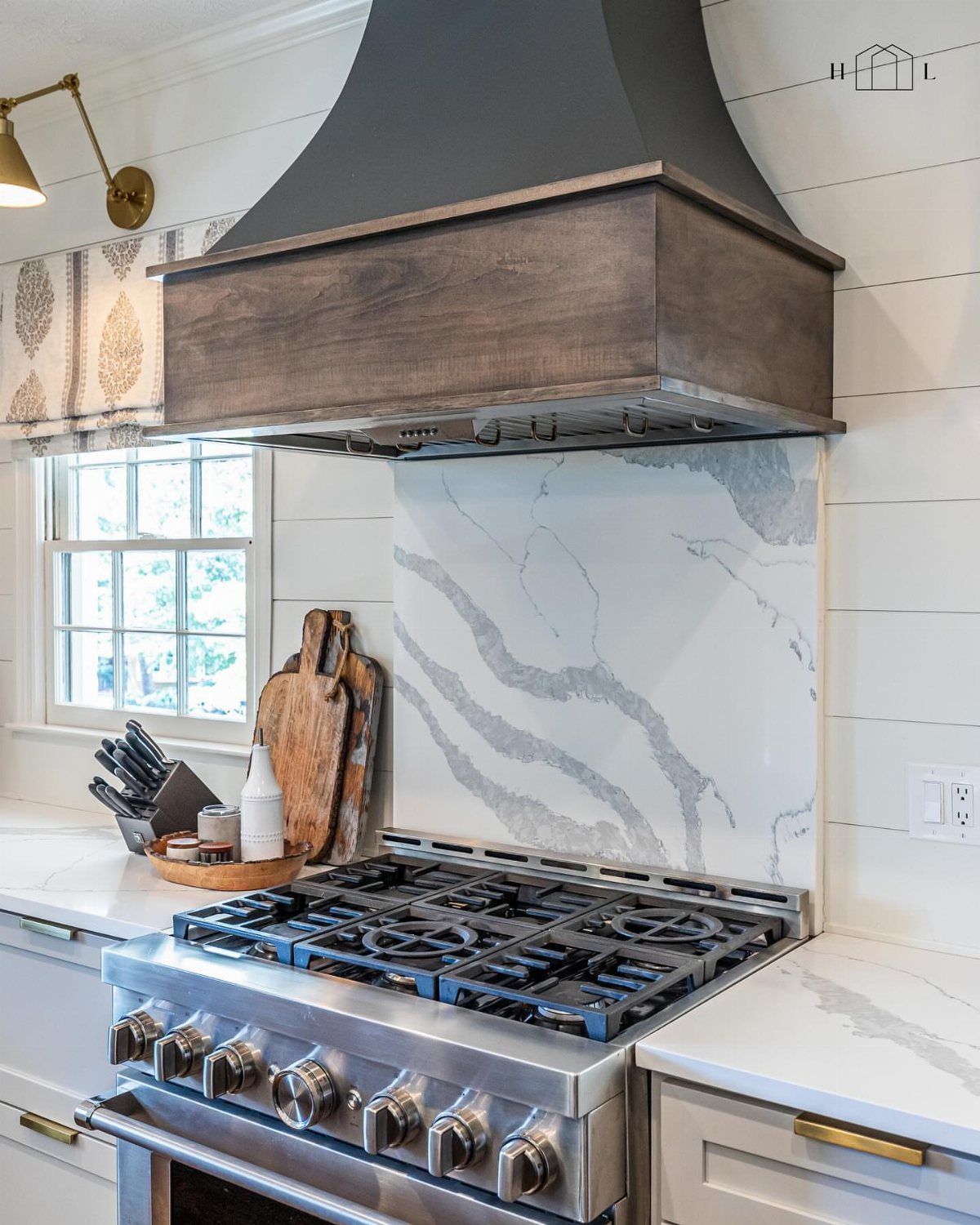Stainless steel gas range with a half-height marble backsplash against white shiplap walls.