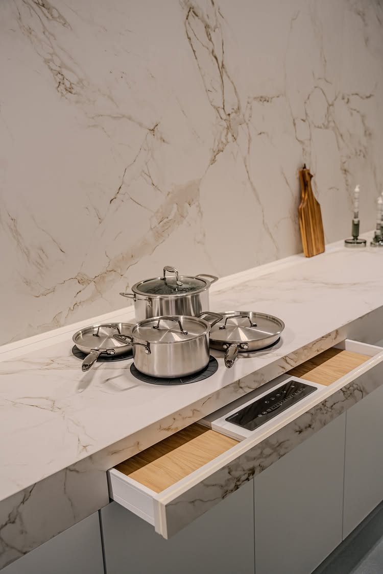 White marble kitchen counter with stainless steel pots and a hidden control drawer.
