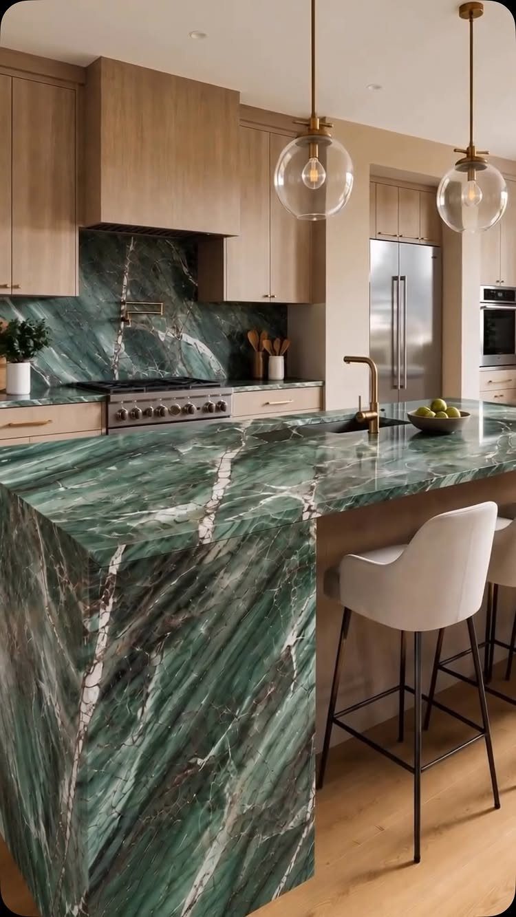 Green veined natural stone island and backsplash in a modern light wood kitchen.