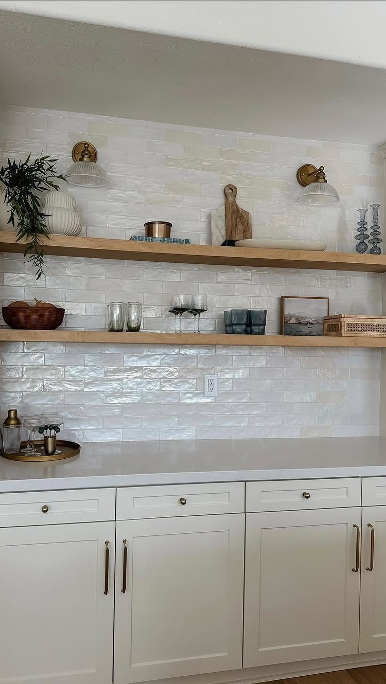 Two light-wood open shelves with glassware and plants against a white tile backsplash.