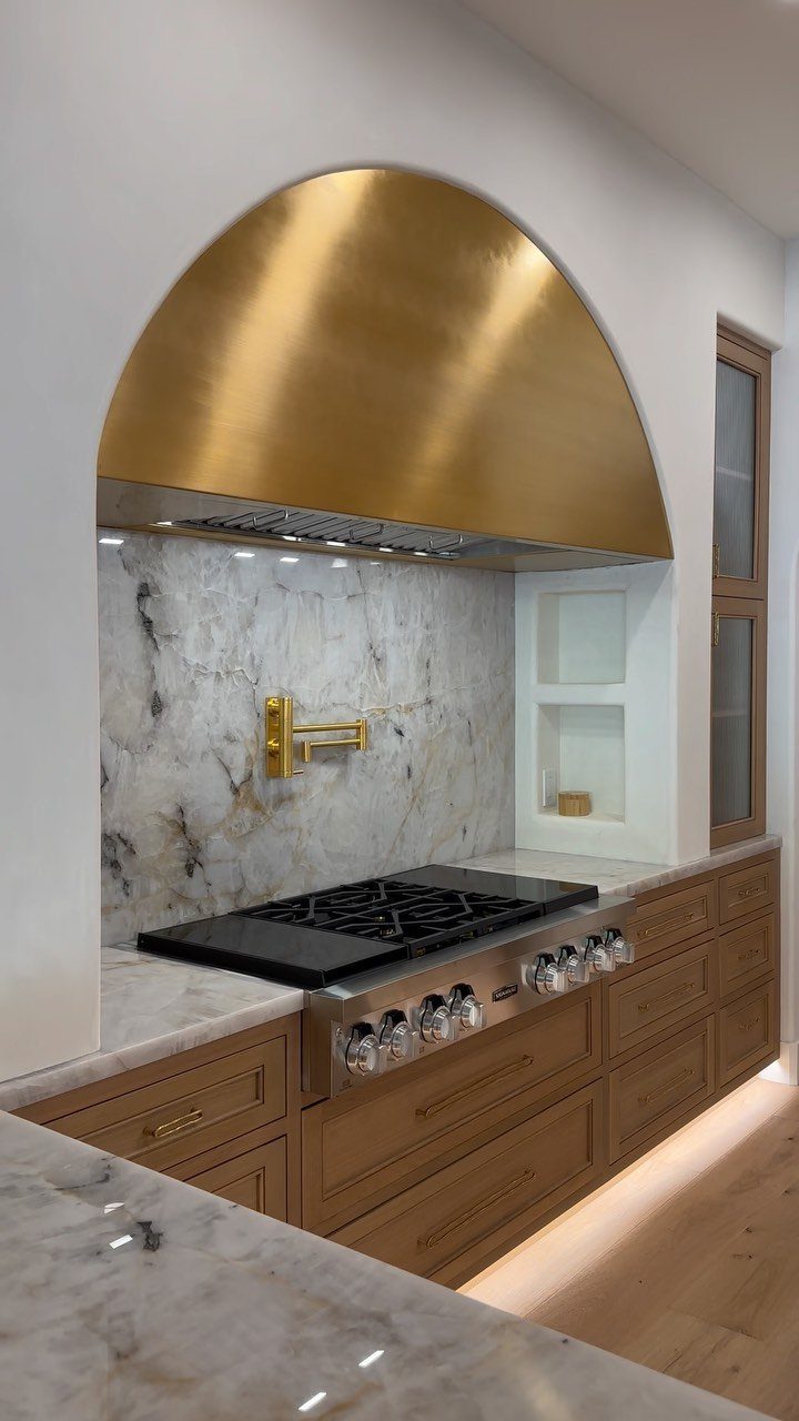 White veined marble countertops and backsplash under a gold arched range hood.