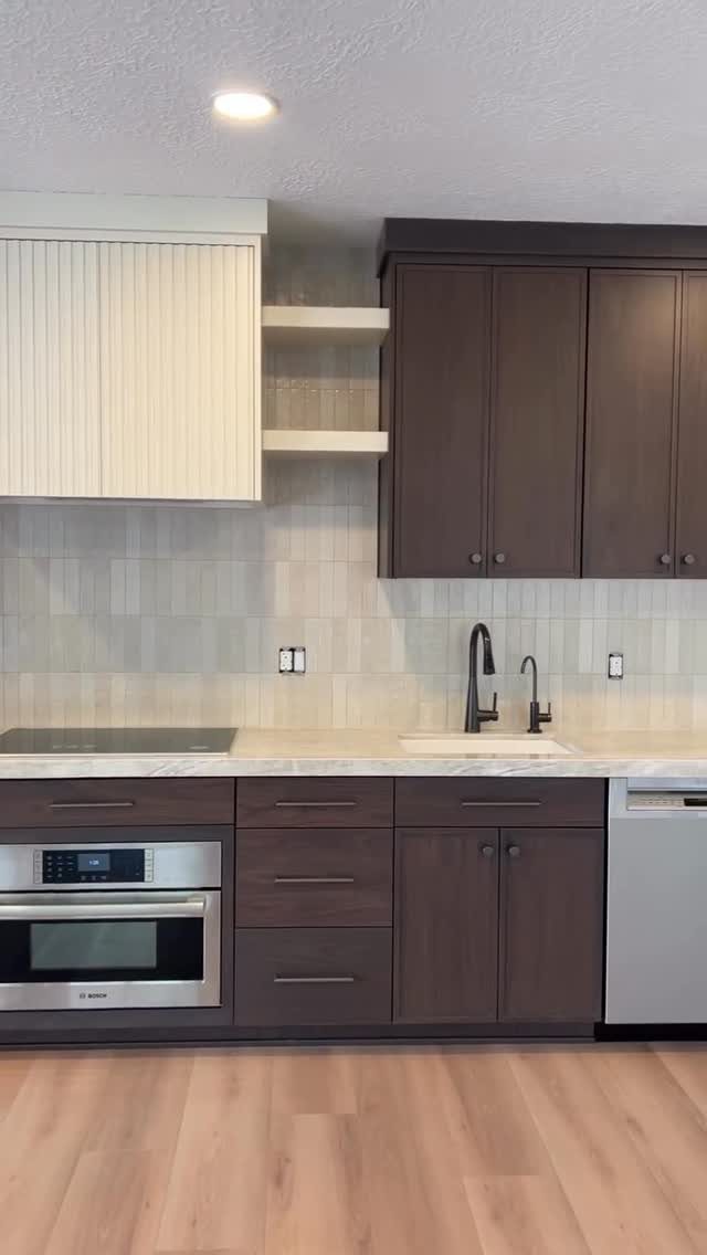 Kitchen cabinets with dark brown wood and one white vertically textured upper cabinet.