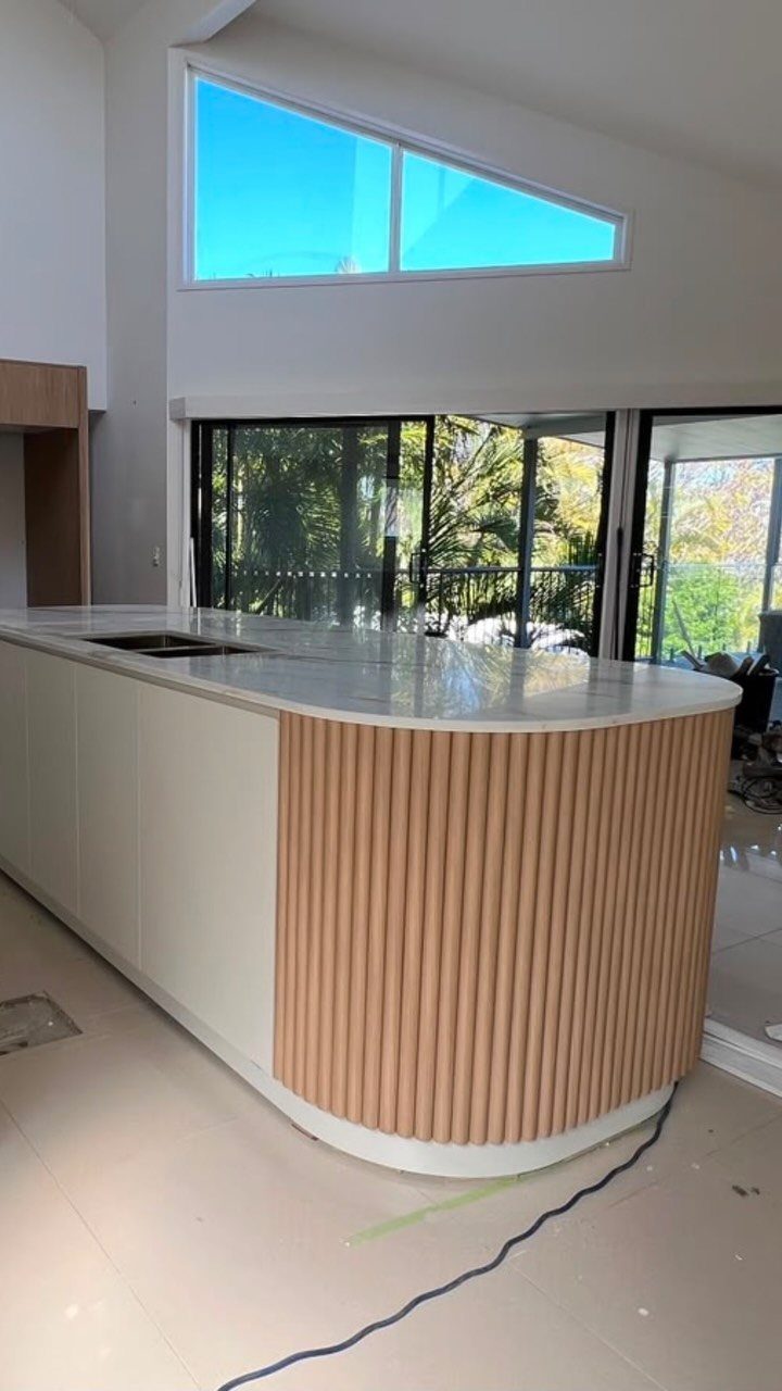 Curved kitchen island with white marble top and vertical wooden slat detailing.